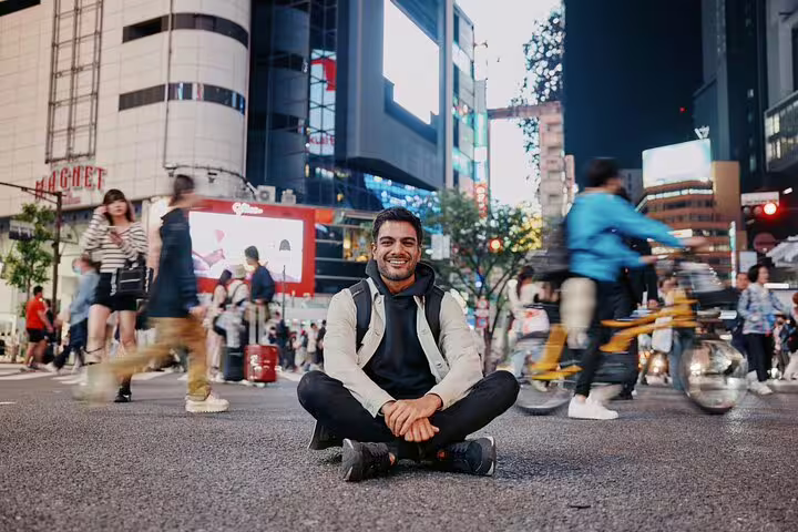 Traveler sitting at Shibuya Crossing at night, Tokyo vacation photographer tour with motion blur street scene