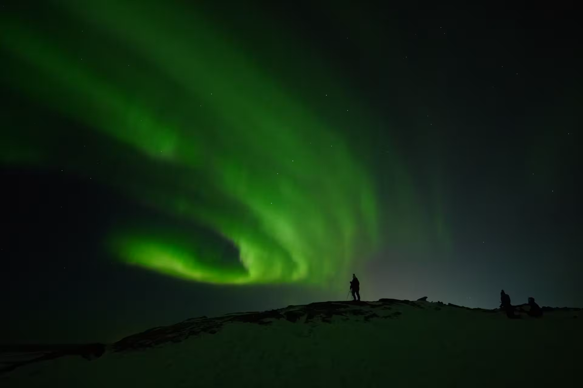 Silhouette of a traveler on a ridge beneath swirling green aurora borealis, ideal Northern Lights and stargazing tour