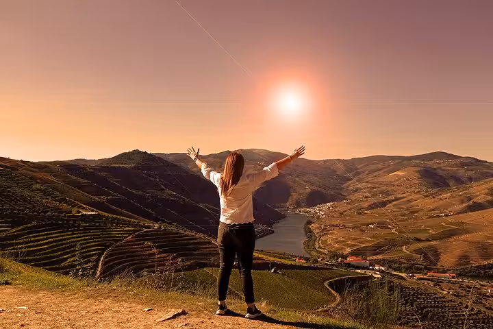 Traveler overlooks terraced vineyards at sunset on a wine trip, with river valley views and golden-hour scenery