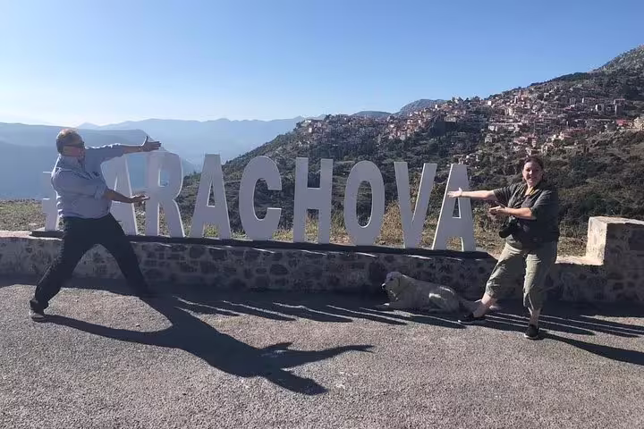 Two travelers pose by the Arachova sign with scenic mountain views during a private day trip from Athens to Delphi.