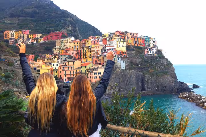 Two travelers celebrate with arms raised overlooking colorful Manarola, Cinque Terre on a day trip from Florence.