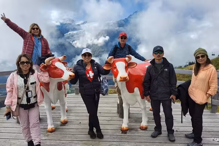 Travelers posing with Swiss cow statues at an alpine viewpoint, 4-day Zermatt Jungfrau Region tour