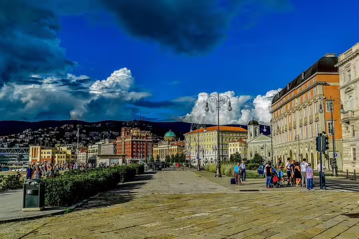 Seafront promenade and colorful historic buildings of Trieste with tour group and dramatic sky on a private walking tour