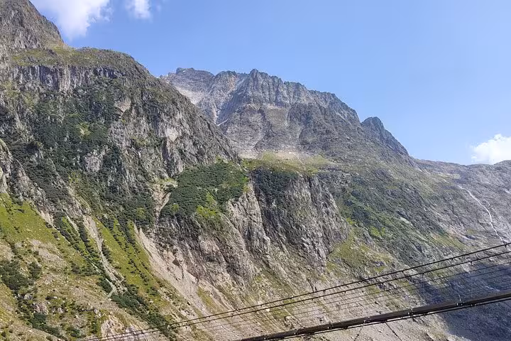 Trift Suspension Bridge on Zurich day trip, spanning a rocky gorge with Swiss Alps peaks and blue sky