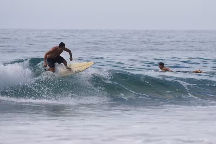 Surfer catching a wave while another swimmer watches in the vibrant waters of Trinidad's beach.