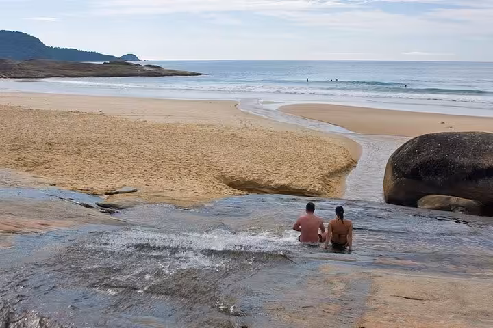Couple relaxing by the waterfall at a serene beach in Trinidad, part of the Nature & Sea tour by Paraty Tours.