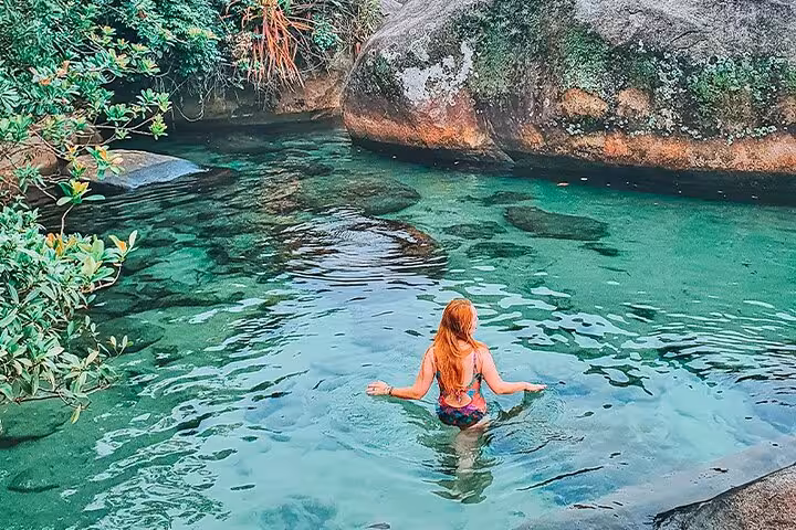 Woman enjoying serene swim in clear natural pool surrounded by lush greenery in Trinidad's scenic beaches.