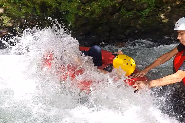 Tubing enthusiast navigating Rio Celeste's lively rapids with splashing water and safety equipment.