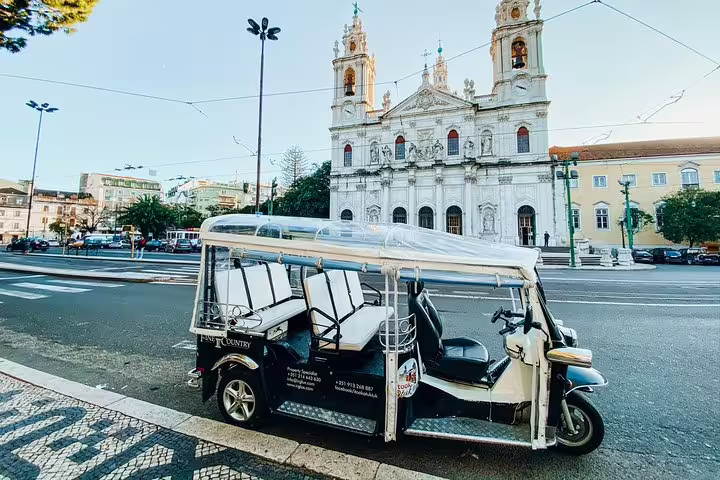 Modern tuk tuk parked near a historic Lisbon church, ready for a Chiado and Bairro Alto sightseeing tour.