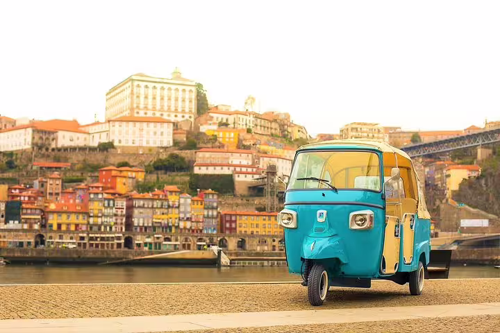 Colorful tuk tuk parked by the Douro River with the stunning historic buildings of Porto, Portugal in the background.