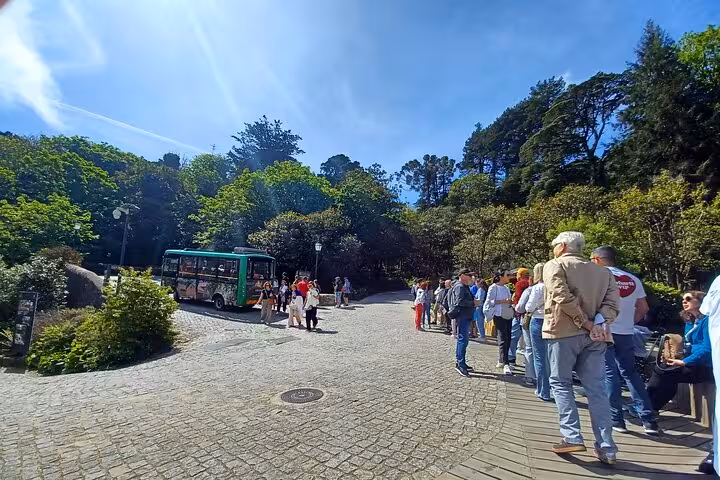Tourists queuing by shuttle stop in Sintra forest park, meeting point for tuk tuk tour to palaces and Cascais