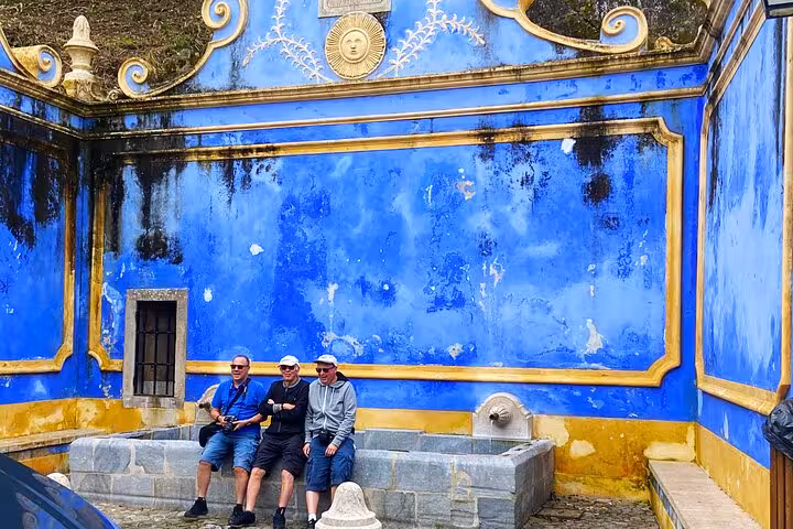Guests relax by the blue and yellow wall at Sintra National Palace on a tuk tuk tour to Cascais coast