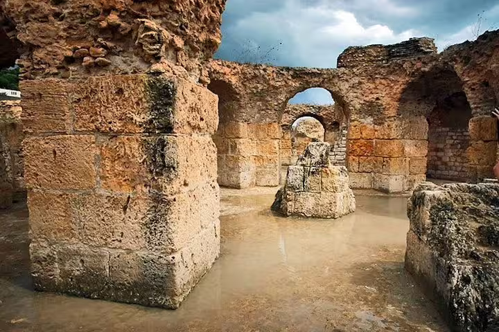 Stone arches and walls of ancient Carthage baths under a dramatic sky, illustrating Tunisia's fascinating archaeological sites.