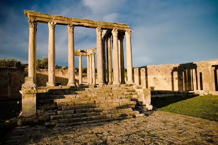 Sunlit Roman columns and steps in the ancient city of Dougga, Tunisia, highlighting historical architecture.