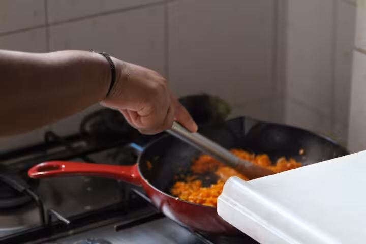Hands stirring sautéed vegetables in pan during Turkish meze cooking class for beginners in Istanbul kitchen