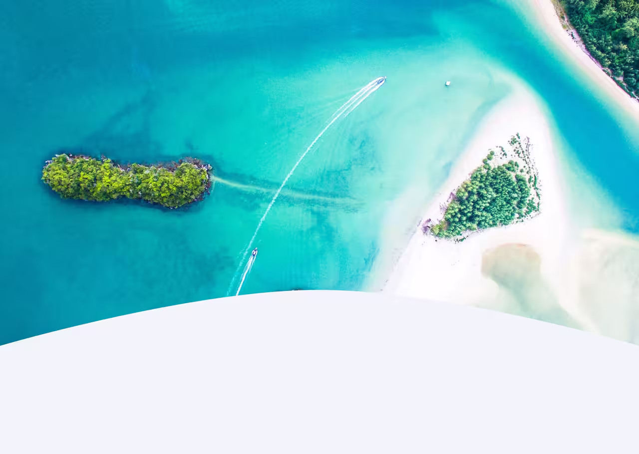 Aerial shot of a turquoise lagoon with lush green islands and a speedboat creating white trails in the water.