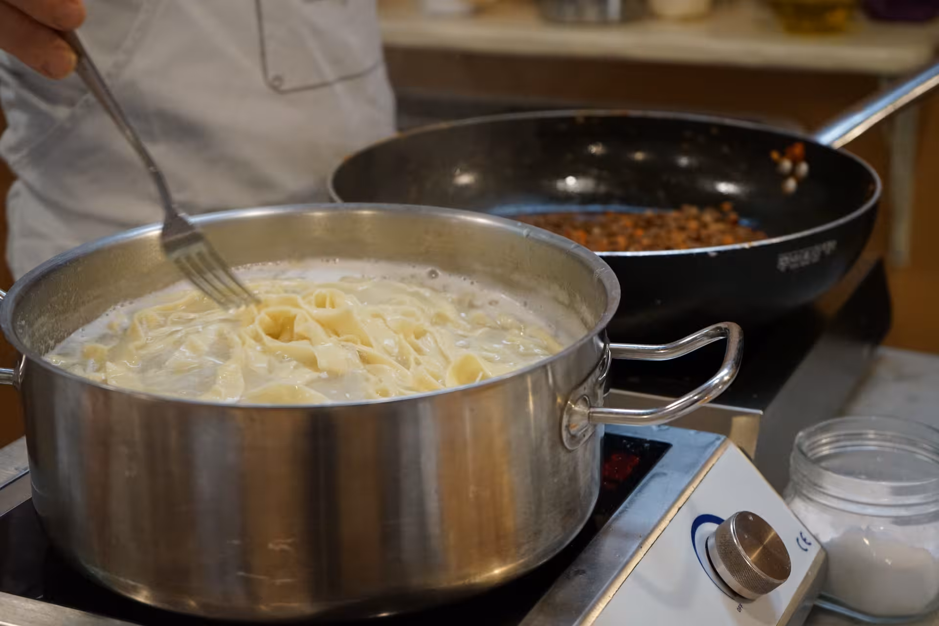 Chef stirring creamy fettuccine in a pot during a hands-on Tuscan cooking class experience in Florence.