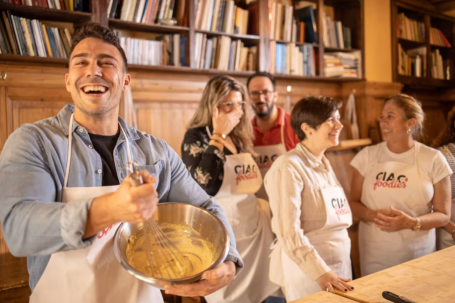 Smiling participants in a Tuscan cooking class, whisking ingredients with joy and camaraderie.