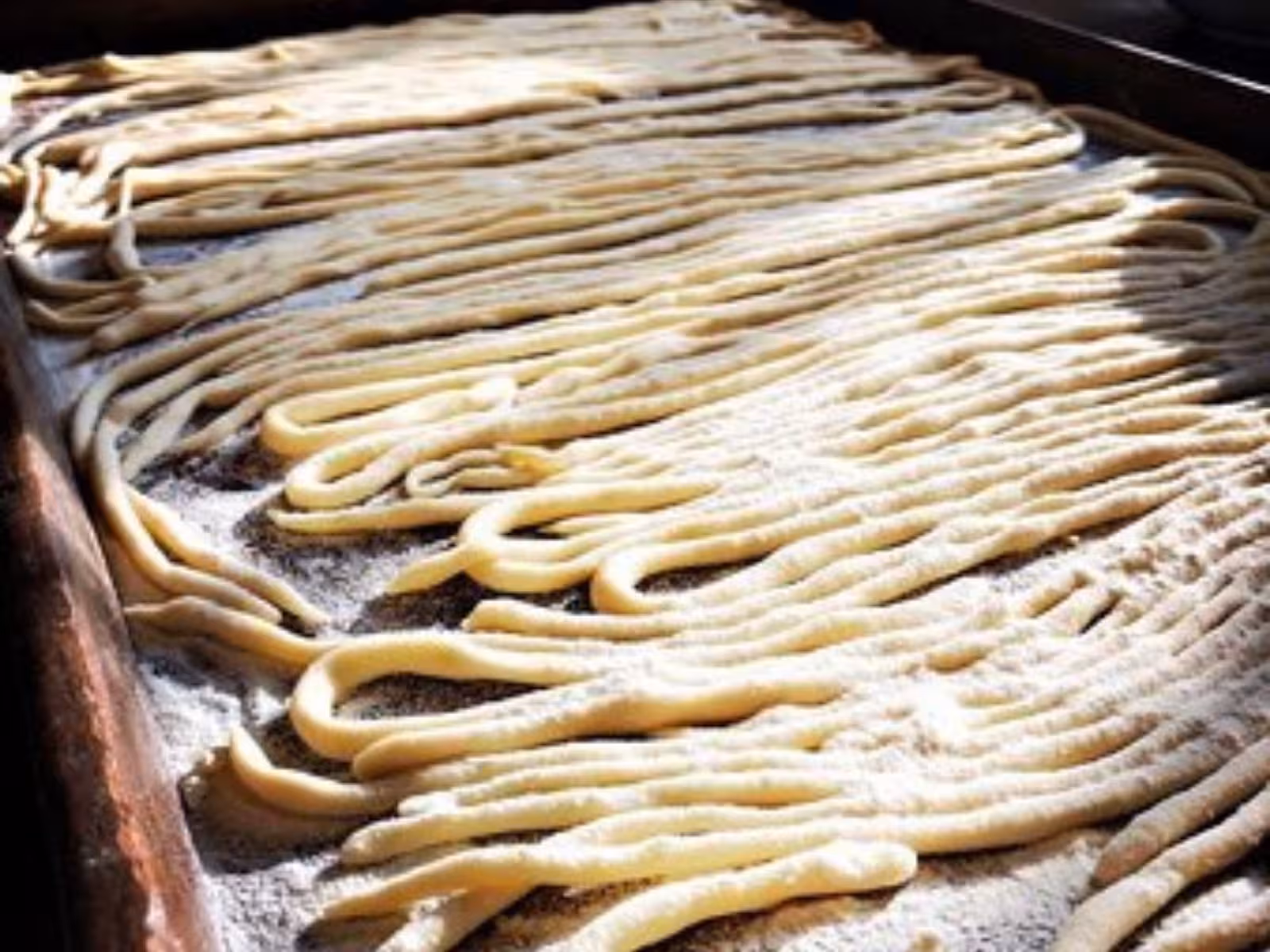 Close-up of freshly made pasta strands drying on a floured surface during a traditional Tuscany farmhouse cooking class.