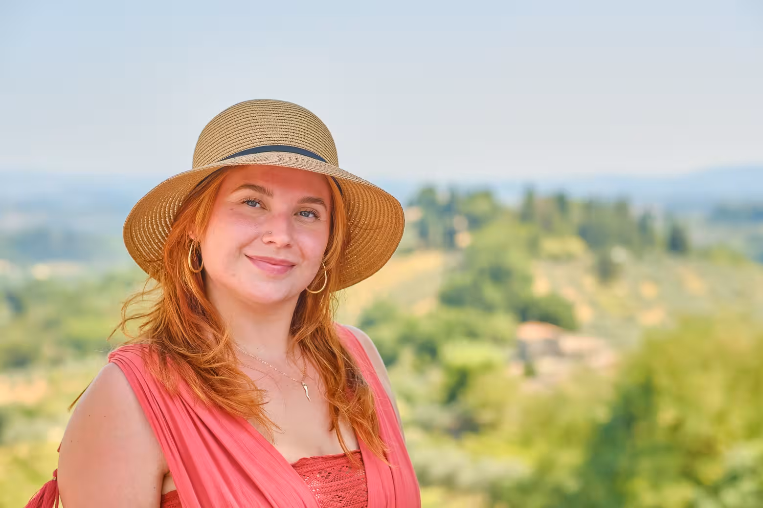 Smiling woman in sun hat enjoying the scenic Tuscan countryside backdrop on a guided tour from Florence.