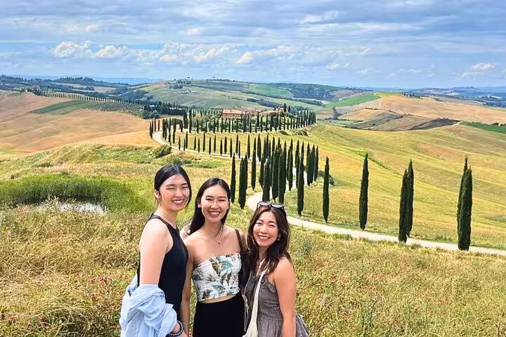 Three travelers enjoying Val D'Orcia's scenic cypress-lined landscape during a small group tour in Tuscany.