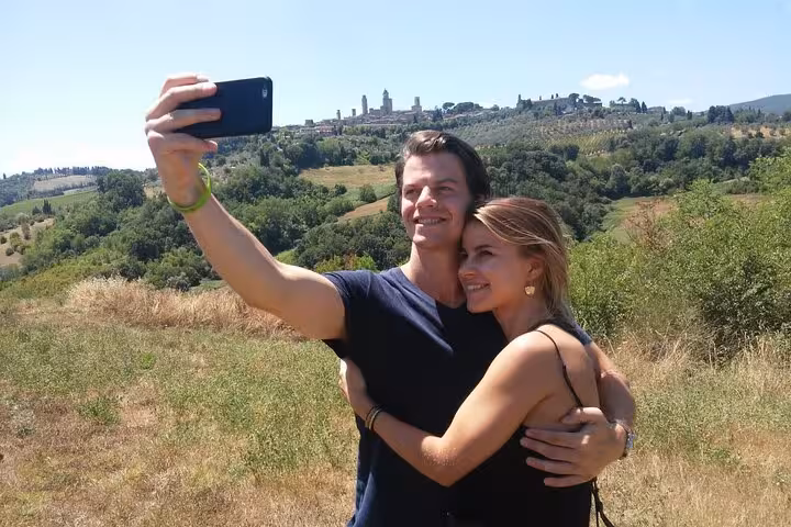 Couple taking a selfie with the scenic backdrop of San Gimignano's towers during a Tuscany Tuk Tuk tour from Florence.