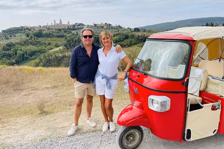 A couple poses with a red tuk tuk overlooking San Gimignano's picturesque landscape on a Tuscany tour.