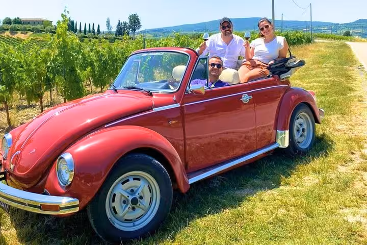 Explore Tuscany in a vintage red Beetle convertible with a scenic vineyard backdrop on our exclusive wine tour.