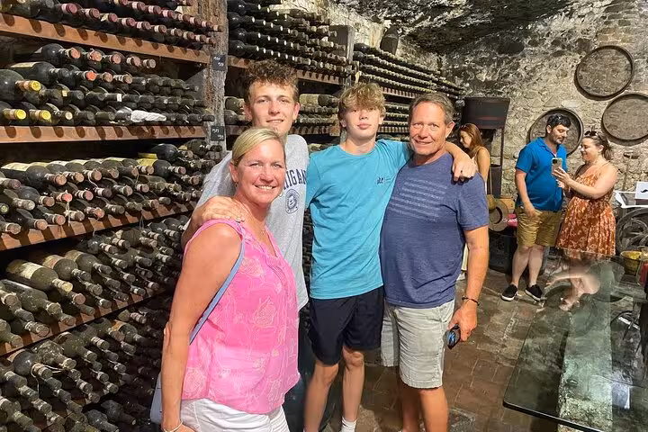 Family exploring a rustic wine cellar filled with vintage bottles on the Tuscany Wine Tour from Rome.
