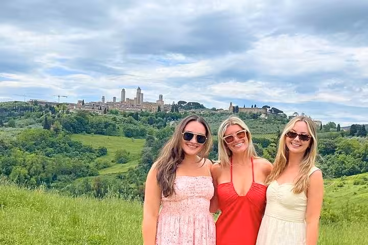 Three friends posing in front of the lush Tuscan countryside and historic San Gimignano during a wine tour from Rome.