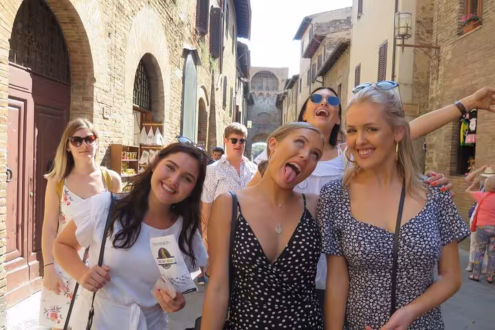 Group of friends smiling and exploring the charming streets of San Gimignano on a wine tour.