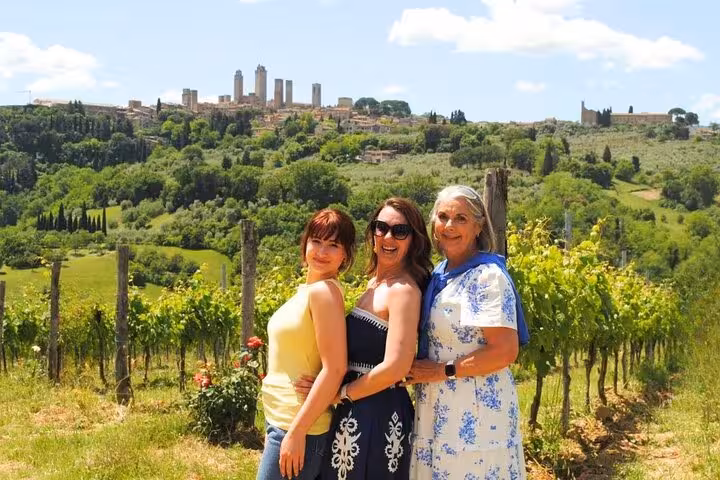 Three women enjoying a sunny day in a vineyard with San Gimignano's towers in the background on a Tuscany wine tour.