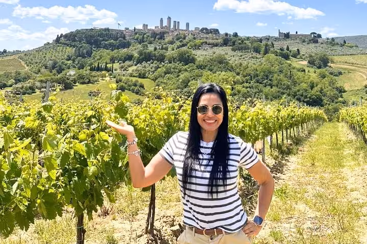 Woman posing in a vineyard with San Gimignano's towers in the background on a Tuscany wine tour from Rome.
