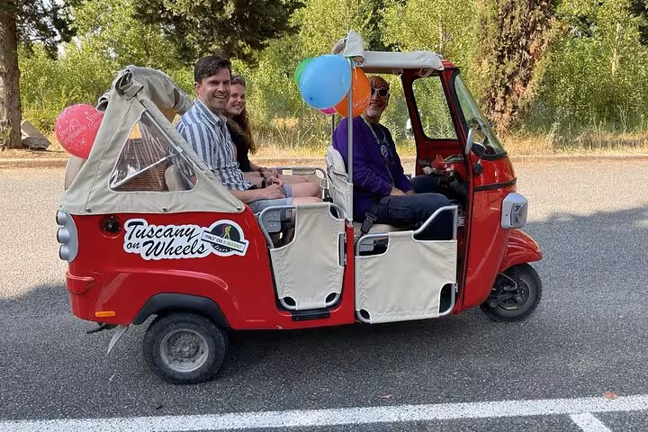 Happy group on Tuscany wine tour by Tuk Tuk, adorned with balloons, enjoying a scenic countryside ride.