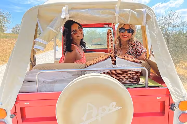 Tour guide engaging with women on a Tuscany wine tour tuk tuk adventure under sunny skies.