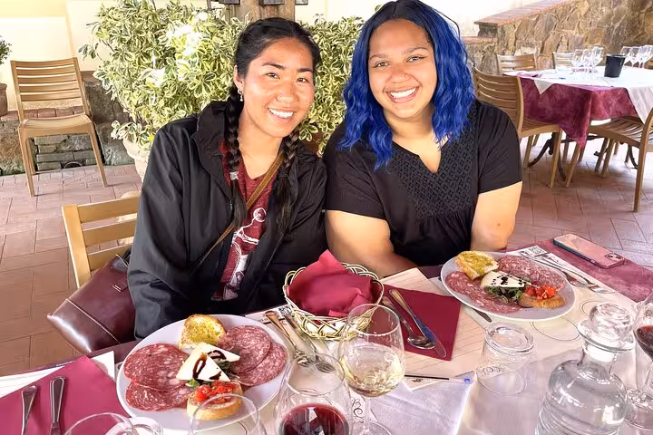 Two smiling women enjoying a Tuscan lunch with charcuterie and wine on a Tuscany wine tour by Tuk Tuk.