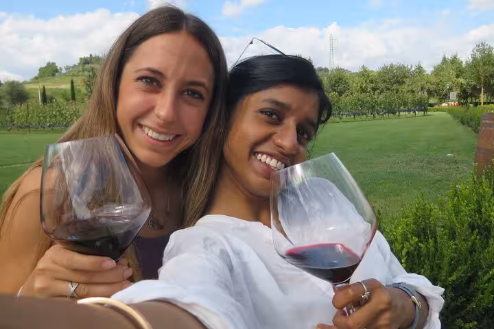 Two friends enjoying a Tuscany wine tour, holding glasses of red wine in a picturesque vineyard setting.
