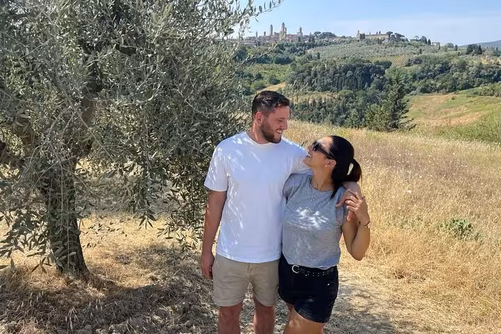 Couple enjoying a Tuscany wine tour by Tuk Tuk, surrounded by scenic vineyards and olive groves under a clear sky.