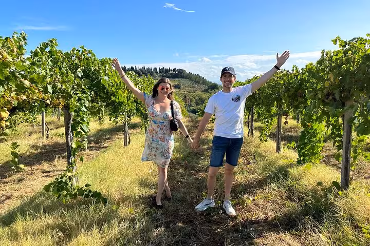 Couple joyfully strolling through lush Tuscany vineyards, enjoying the serene landscape on a private wine tour.