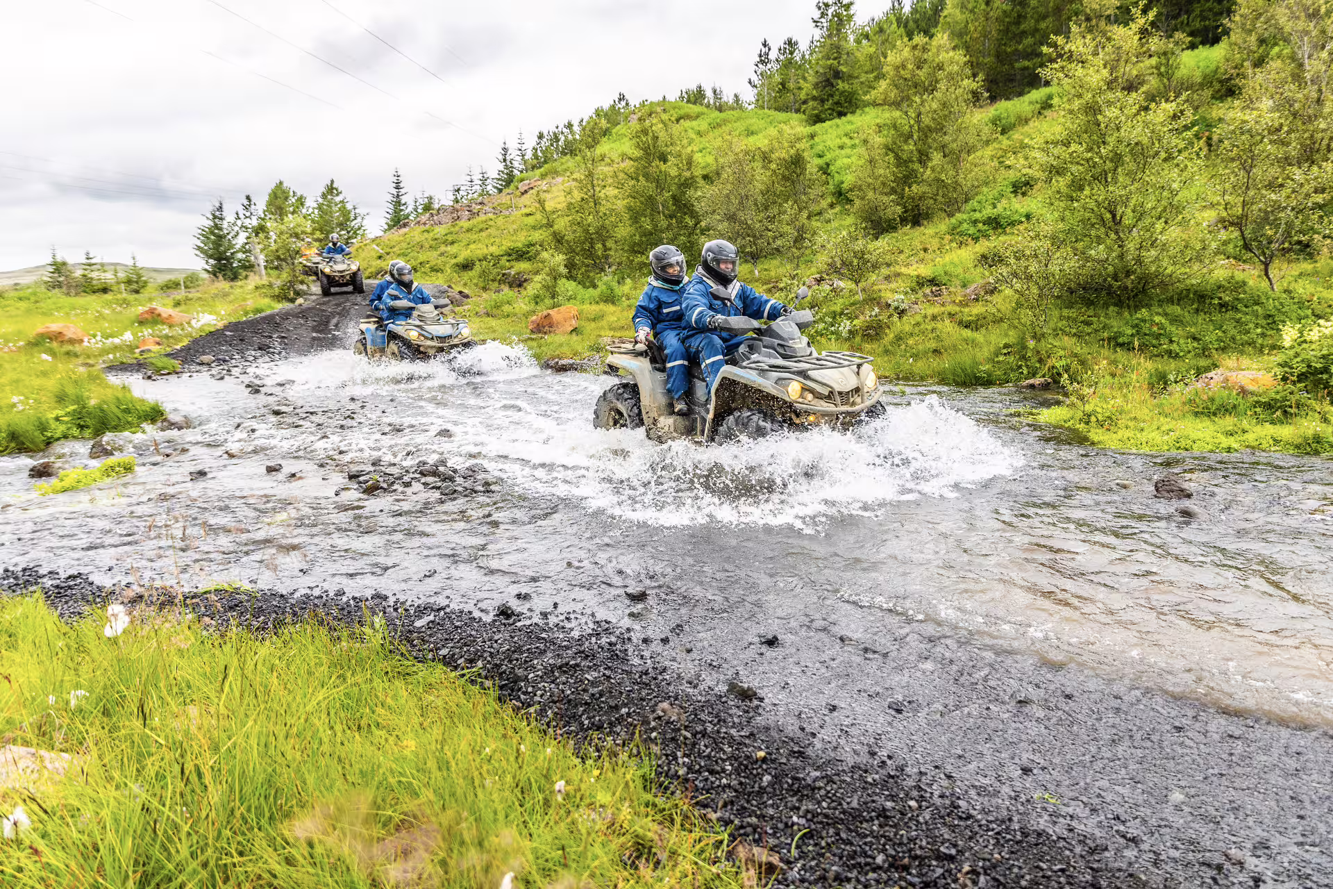 ATV riders navigate a scenic river crossing on the thrilling 2 Hour Twin Peaks adventure through lush, green landscapes.