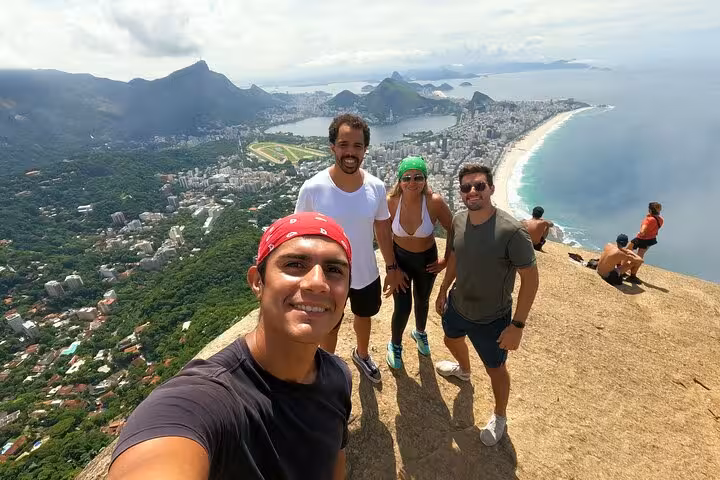 Hikers posing at the peak of Two Brothers Mountain with stunning panoramic views of Rio's coastline and skyline.