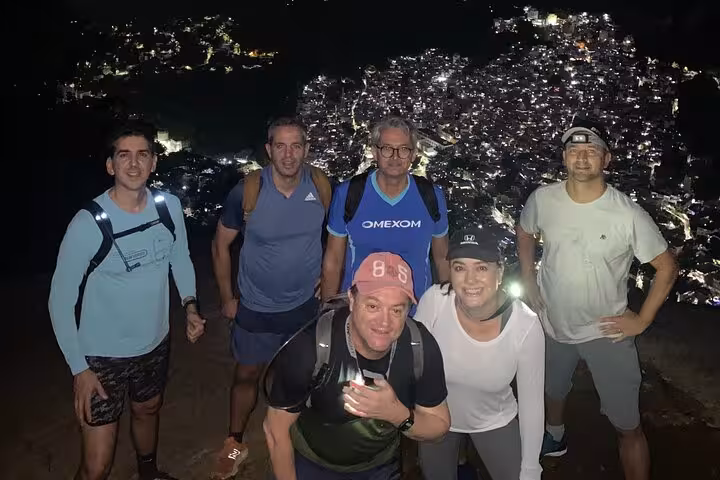 Nighttime hiking group with Rio de Janeiro city lights backdrop at Two Brothers Mountain summit.