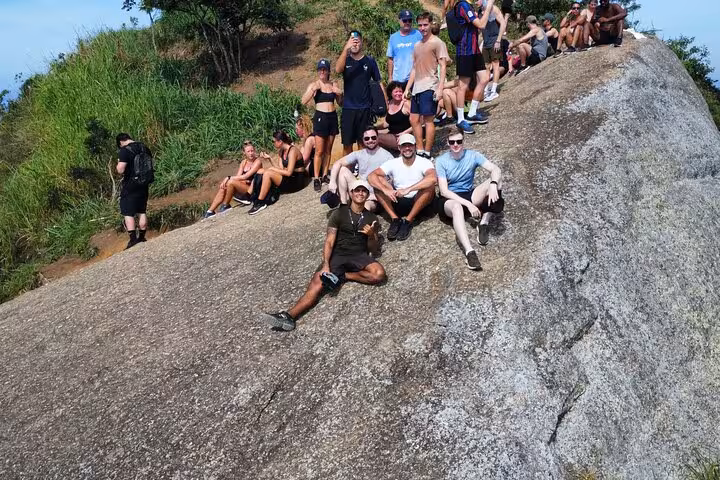 Group of hikers relaxing on a rocky ledge during the Two Brothers hike, offering panoramic views of Rio.