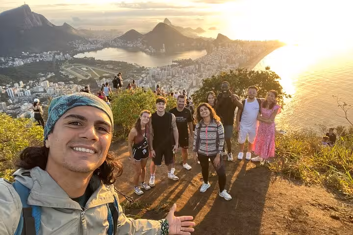 Happy hikers pose with breathtaking Rio de Janeiro landscape at Two Brothers peak, offering panoramic city views.
