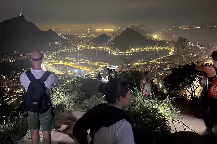 Nighttime view from Two Brothers peak shows Rio de Janeiro city lights illuminating the landscape below hikers.