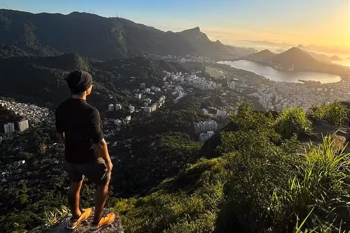 Solo hiker admiring sunrise over Rio from Two Brothers hike in Vidigal, capturing the serene beauty of the landscape.