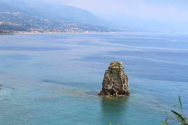 Solitary sea stack rises from turquoise Tyrrhenian waters with coastal villages in the distance on a Cosentino historical walking tour