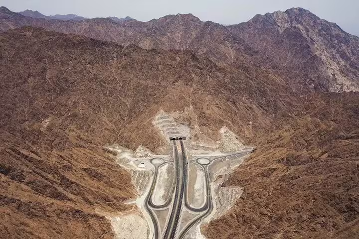 Aerial view of a scenic mountain highway in the UAE, featuring a tunnel entrance on the Full-Day Six Emirates Tour.