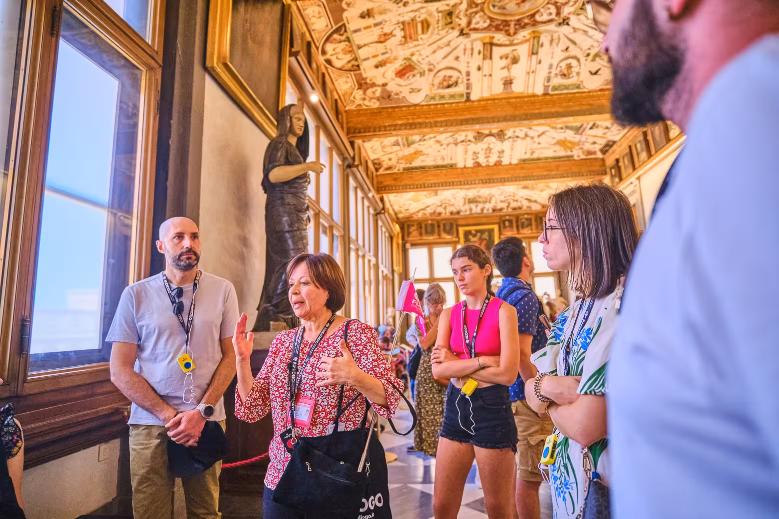 Tour guide explaining art to a small group inside the Uffizi Gallery with ornate ceilings and historic sculptures.
