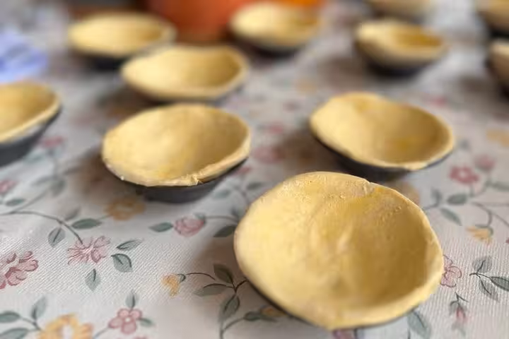 Unbaked pastry shells arranged on a floral tablecloth, ready to be filled for Pastel de Nata.